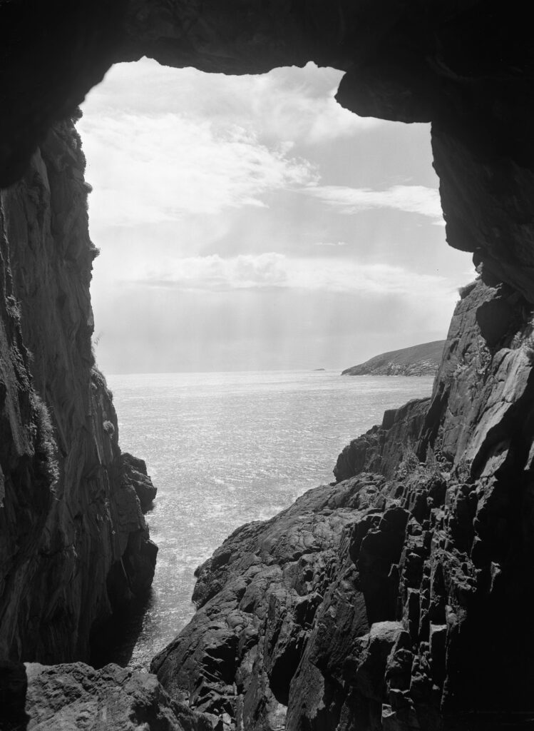 Black and white photographs. Cliffs on either side of the frame, and the sea in the middle in the background.